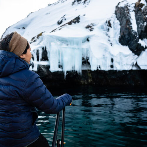 Woman looking at a cliff face with ice and snow from the boat - Photo by Alex Savu - Visit Greenland