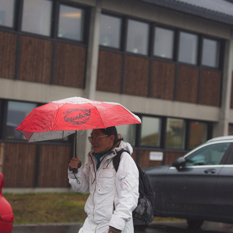 Greenlandic lady holding red umbrella in the rain